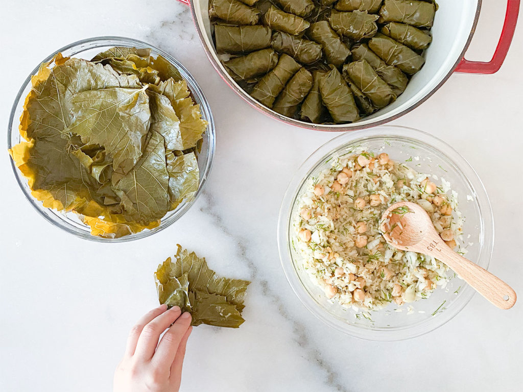 Stuffed grape leaves in a pot, grape leaves in a bowl, rice and chickpea filling in a bowl and rolling grape leaves