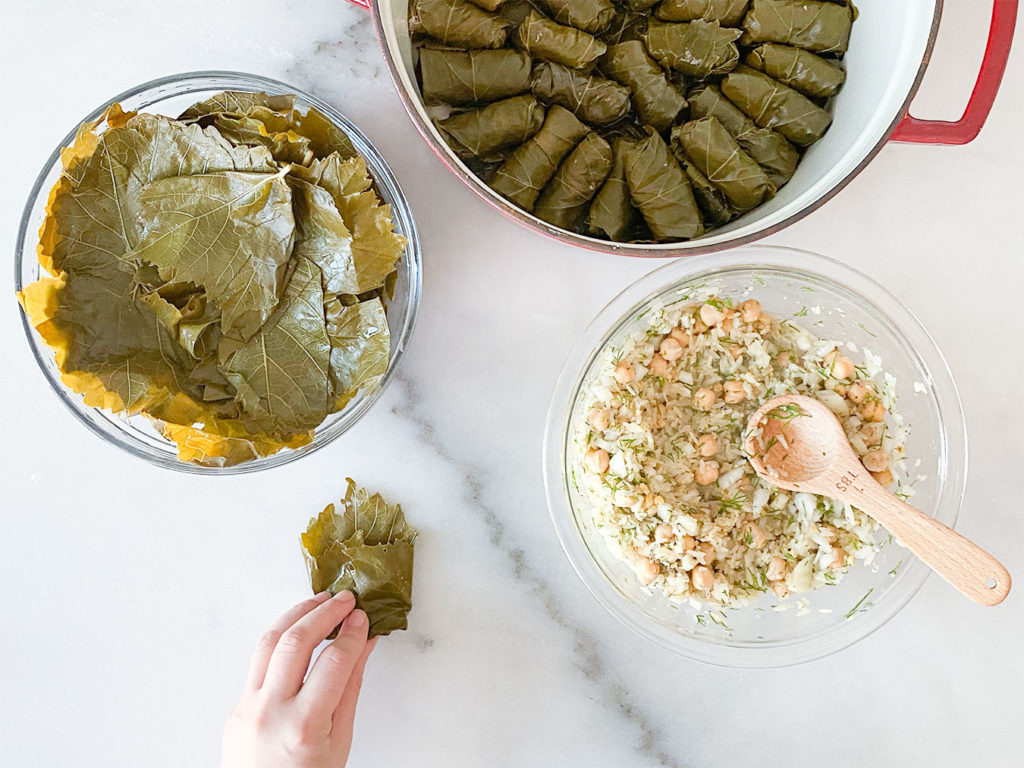 Stuffed grape leaves in a pot, grape leaves in a bowl, rice and chickpea filling in a bowl and rolling grape leaves