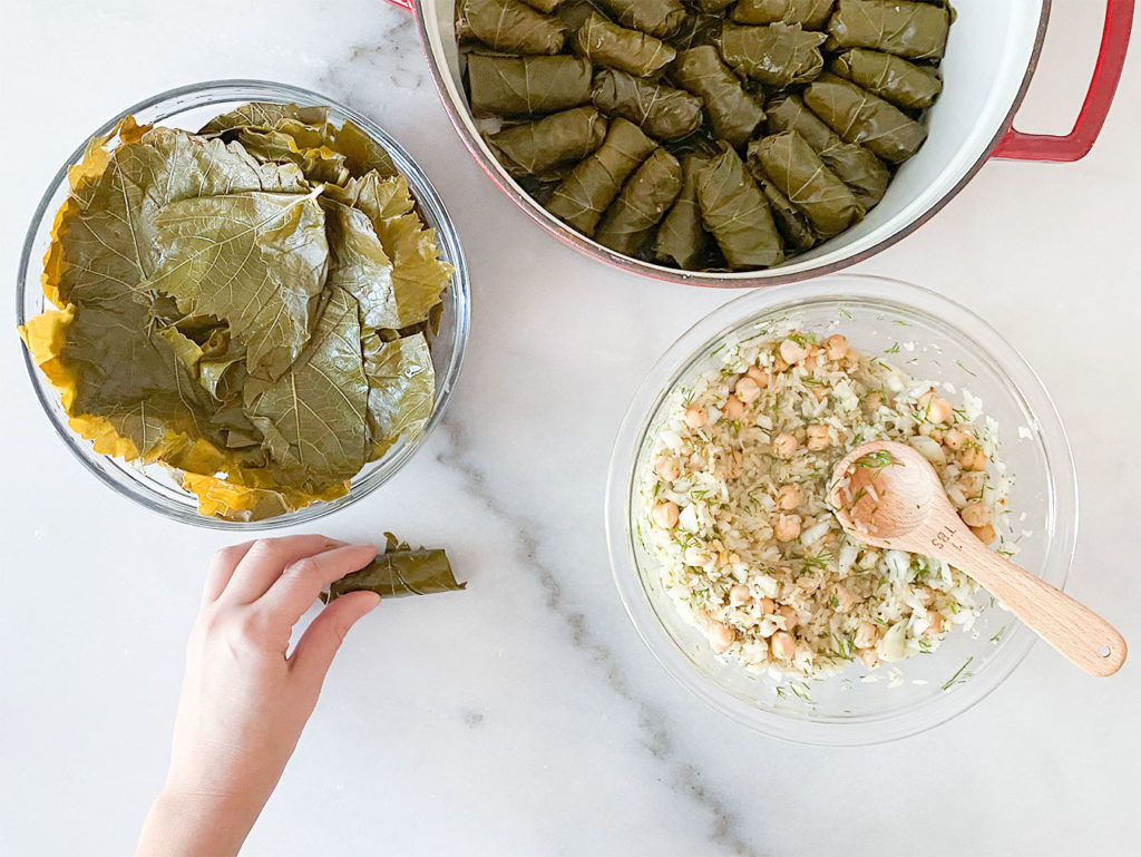 Stuffed grape leaves in a pot, grape leaves in a bowl, rice and chickpea filling in a bowl and rolling grape leaves