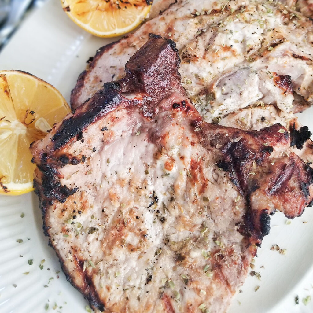 Grilled Greek Yogurt Marinated Pork Chops on a plate with grilled lemons