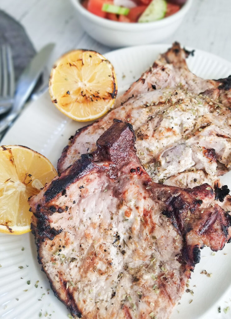 Grilled Greek Yogurt Marinated Pork Chops on a plate with grilled lemons