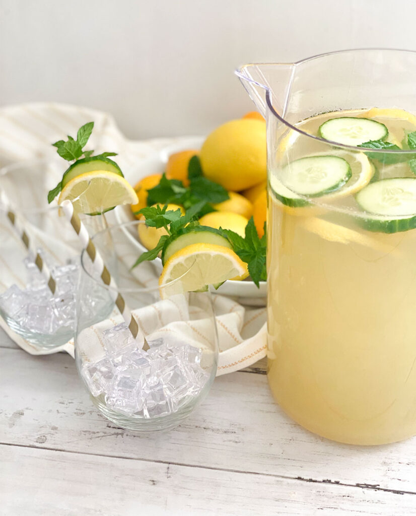 Cucumber Mint Lemonade in a pitcher with a bowl a lemons and glasses filled with ice