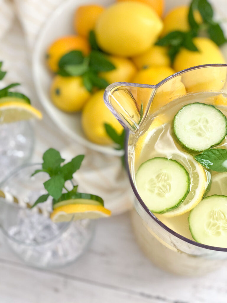 Cucumber Mint Lemonade in a pitcher with a bowl a lemons and glasses filled with ice