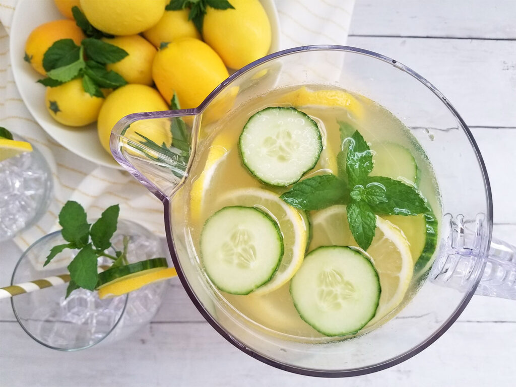 Cucumber Mint Lemonade in a pitcher with a bowl a lemons and glasses filled with ice