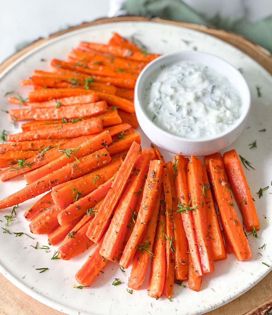 Baked carrot sticks on a plate with a side of tzatziki sauce