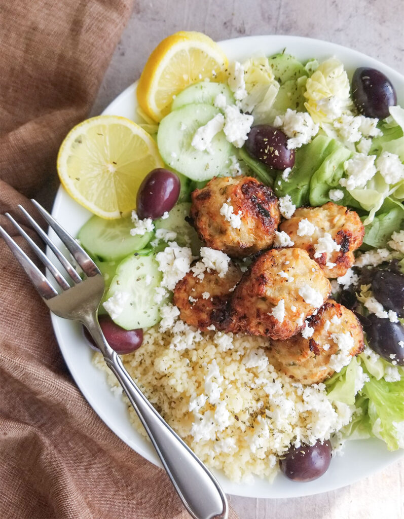 chicken meatballs on top of couscous and salad greens