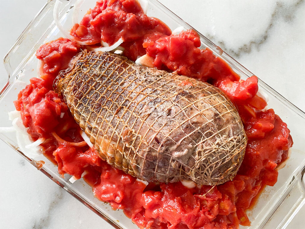 browned leg of lamb with sliced onions and diced tomatoes