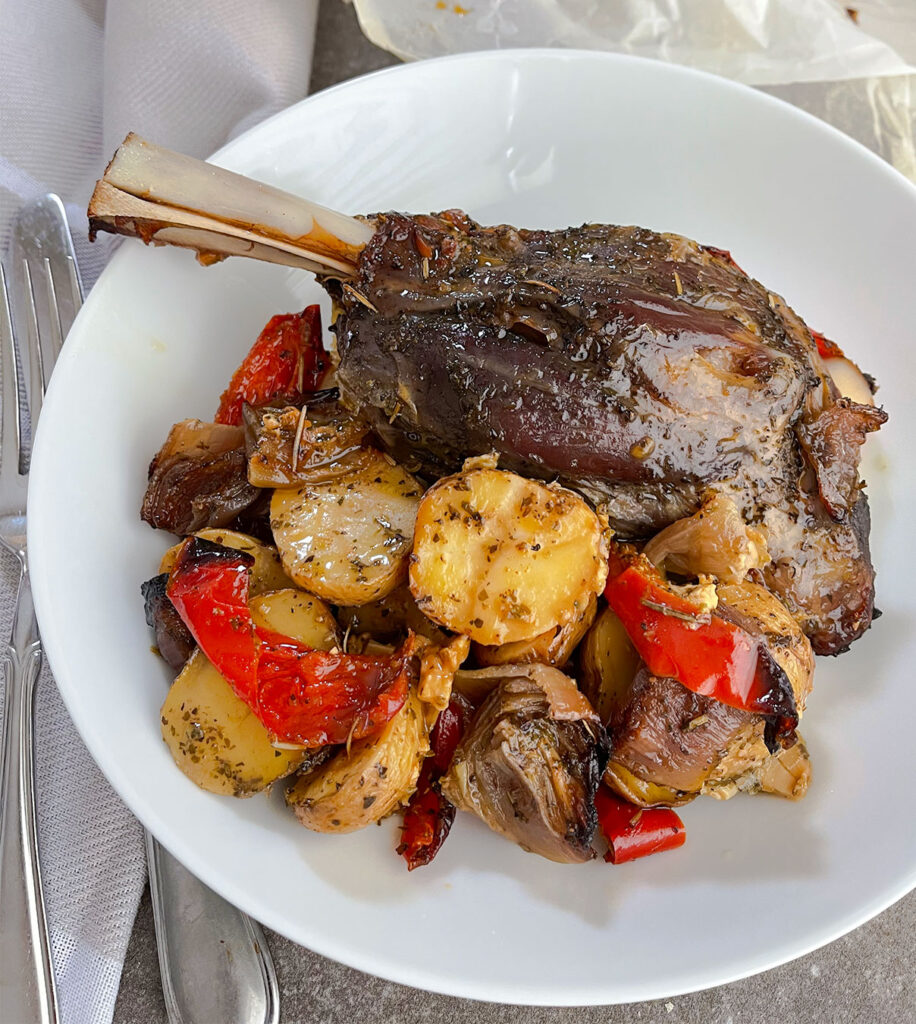 Roasted lamb shank with potatoes, peppers and onions