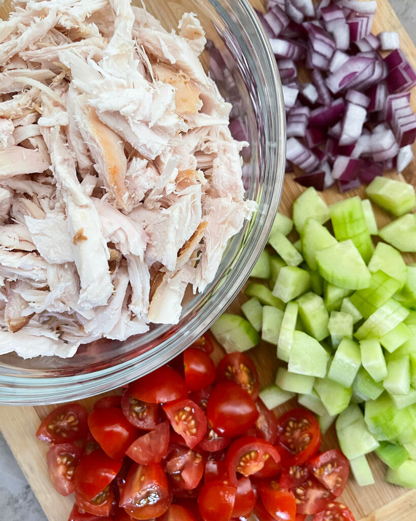 rotisserie chicken in a bowl, chopped cucumbers, tomatoes and red onion