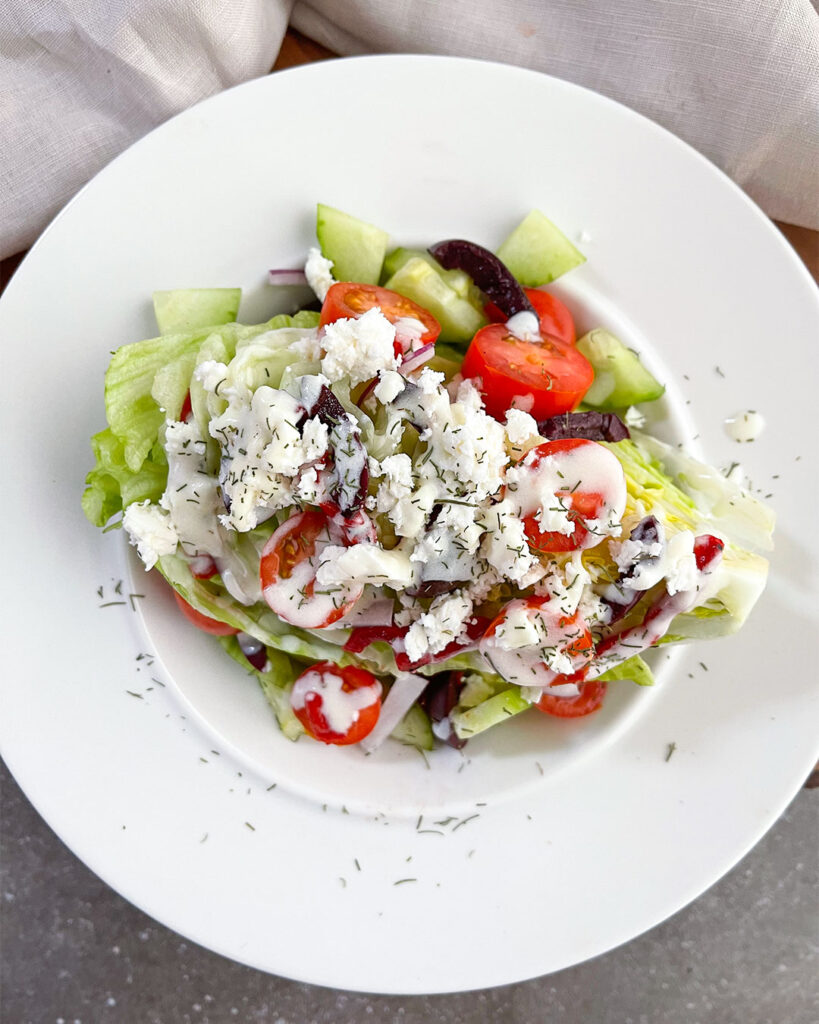 Iceberg lettuce wedge salad topped with tomatoes, cucumbers, onions, feta cheese and dill