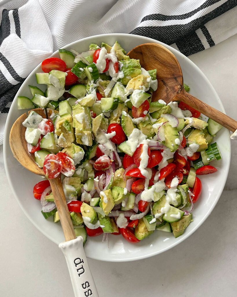 A white bowl with a chopped Avocado, Cucumber, Tomato drizzled with a creamy white feta dressing