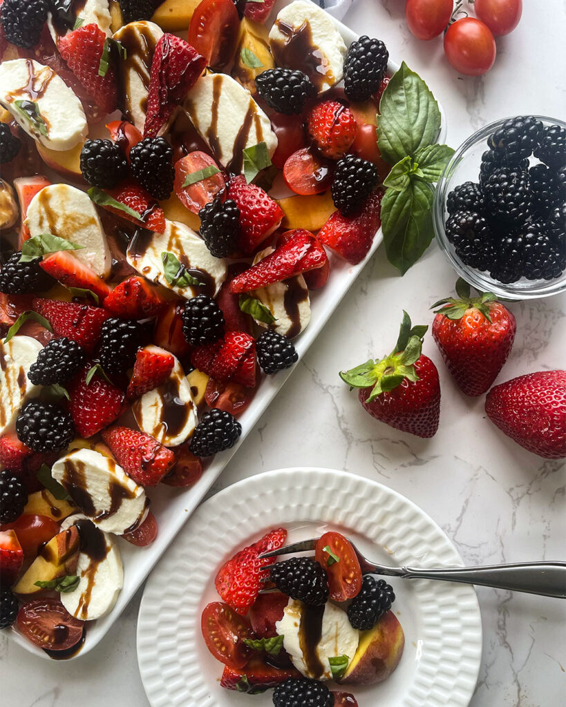 A white platter with an arrangement of peaches, juicey strawberries, and blackberries drizzled with a balsamic glaze.