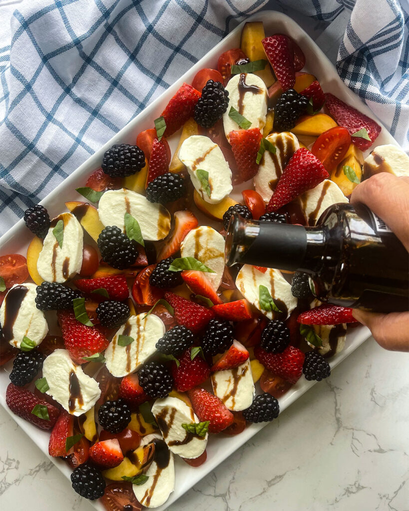 A picture showing drizzling balsamic vinegar on a fruit salad.