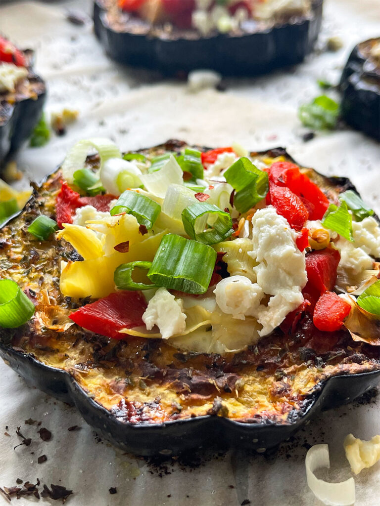 Sunrise Squash: Roasted acorn squash rings with sunny-side-up eggs, red peppers, artichoke hearts, feta cheese, and green onions on a plate