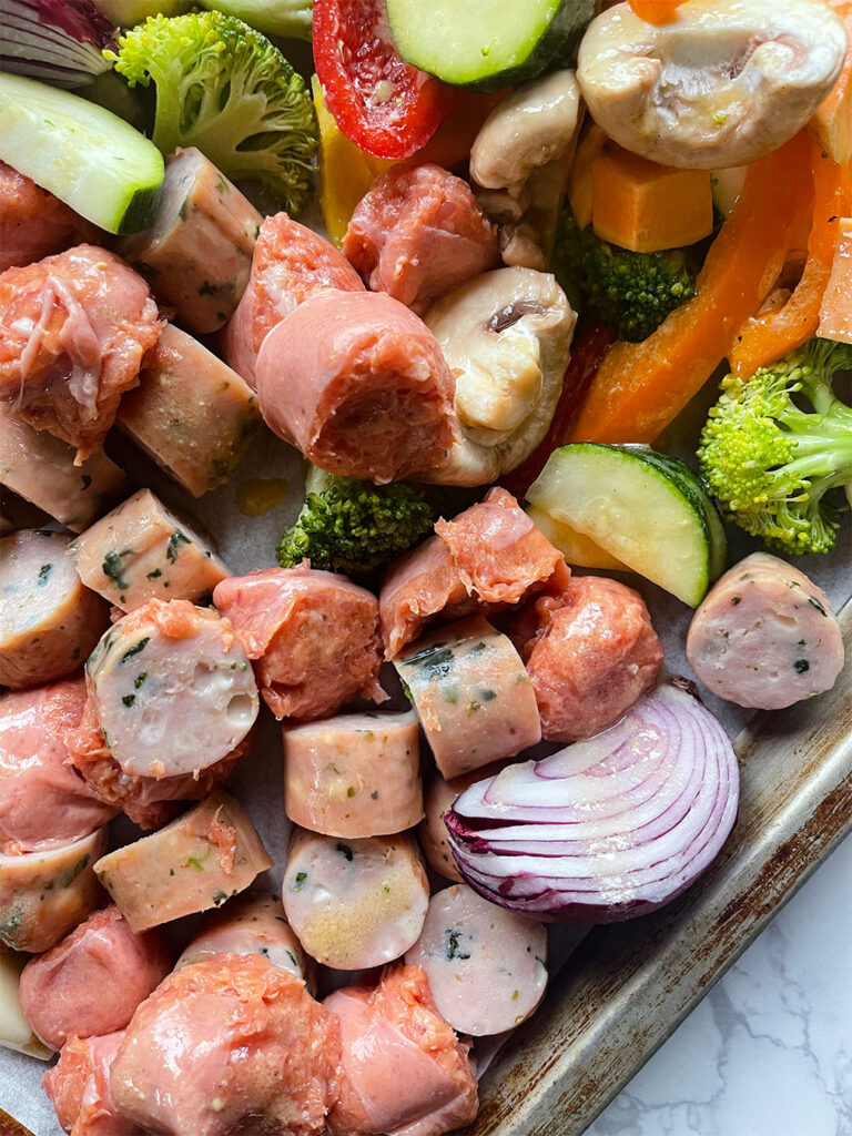 Sheet pan with uncooked sausage and vegetables ready for the oven.