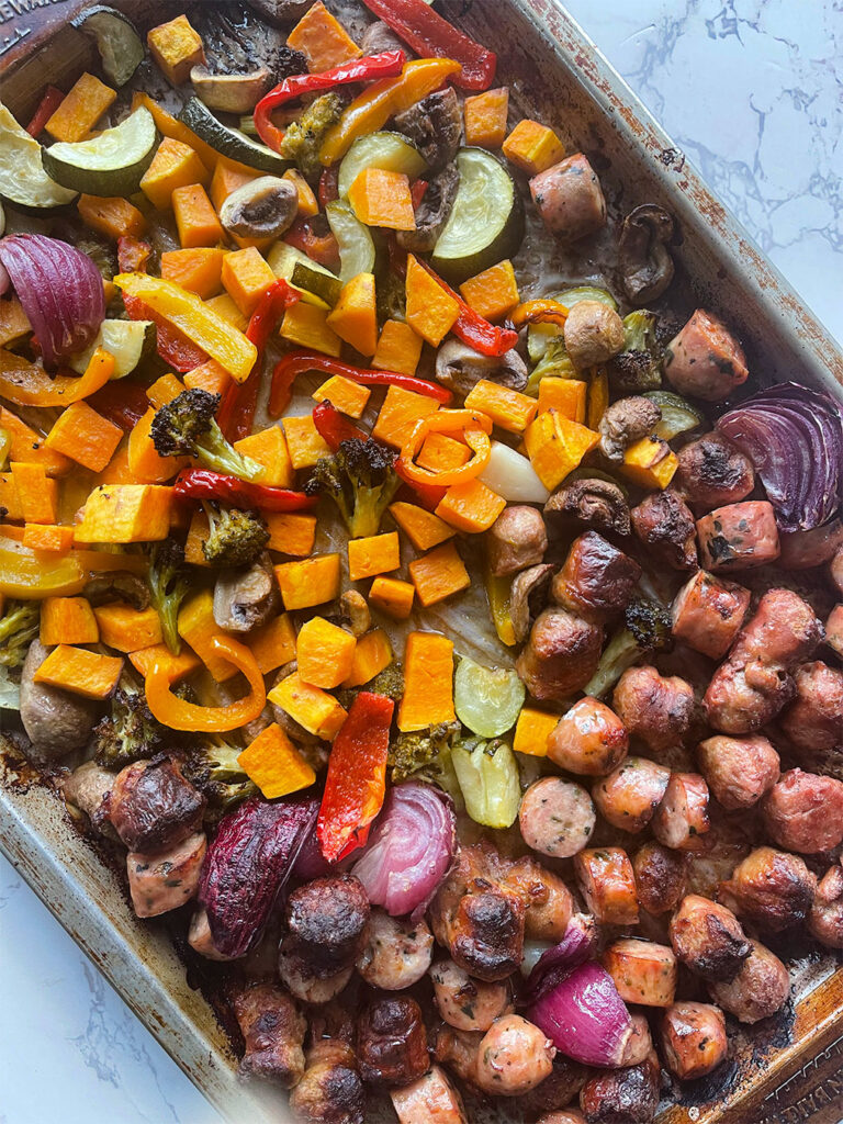 A sheet pan with cooked sausage and vegetables.