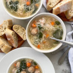 Steaming bowl of Italian Wedding Soup, a comforting mix of savory meatballs, tender vegetables, and hearty broth, served in a pristine white bowl alongside slices of crusty bread