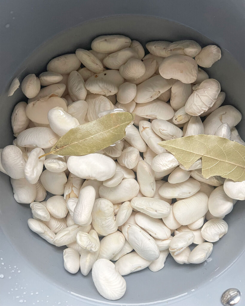 Gigantes beans soaking in sauce pan covered with water and bay leaves