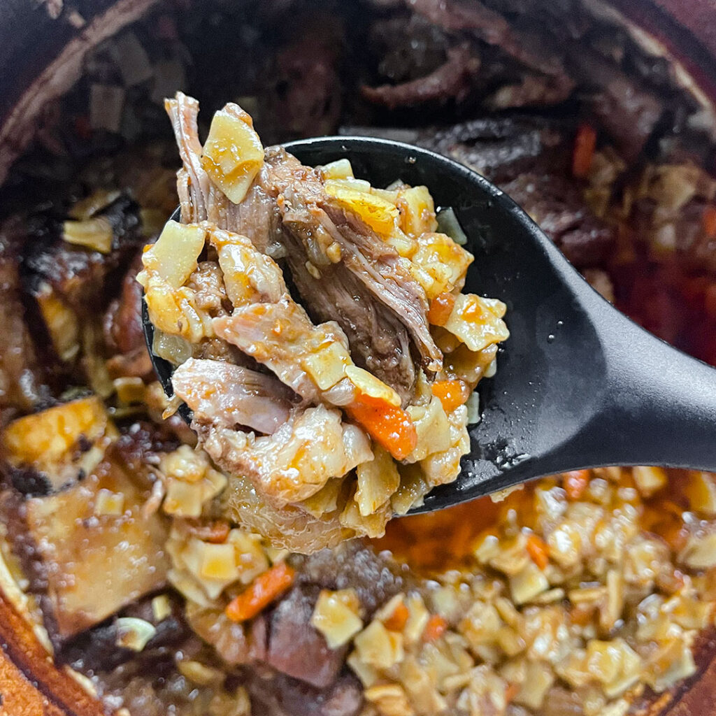 A spoon of hilopites taken from the pot of slow cooked short ribs.
