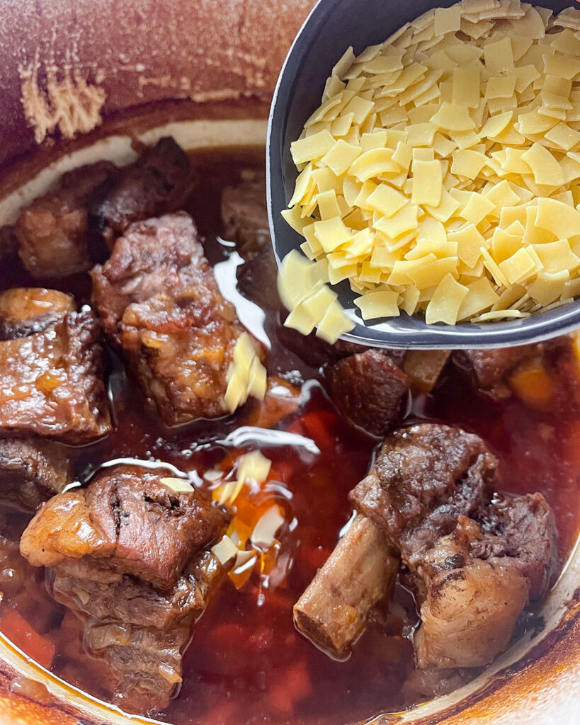 Adding the hilopites (pasta) to the pot of short ribs.